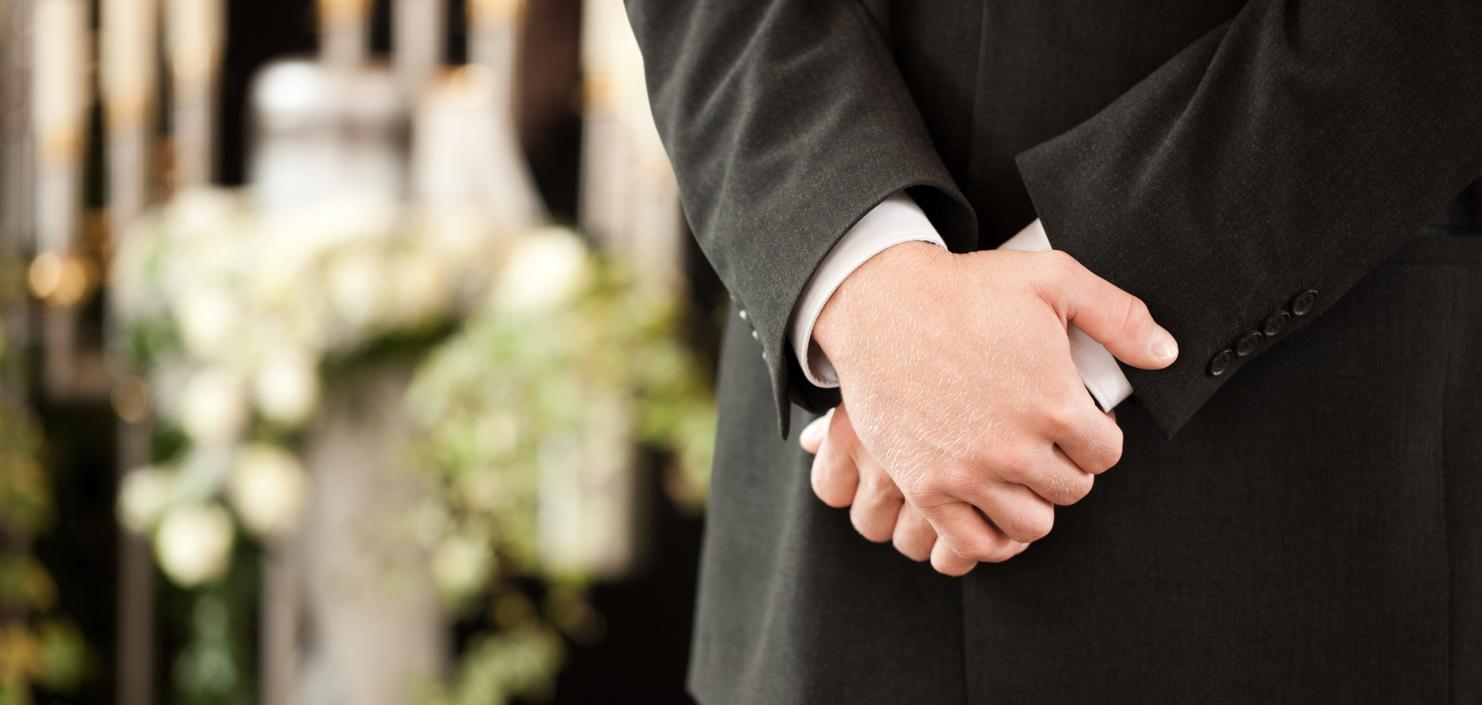 Ein Mann in einem Anzug steht mit verschränkten Händen vor einer dekorierten Kulisse mit Blumen und Kerzen.