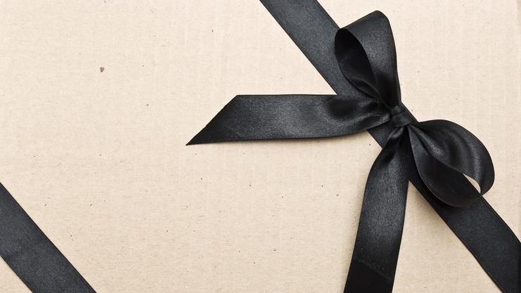 Geschenk mit schwarzem Satinband auf braunem Kraftpapier. Das Band ist zu einer Schleife gebunden.