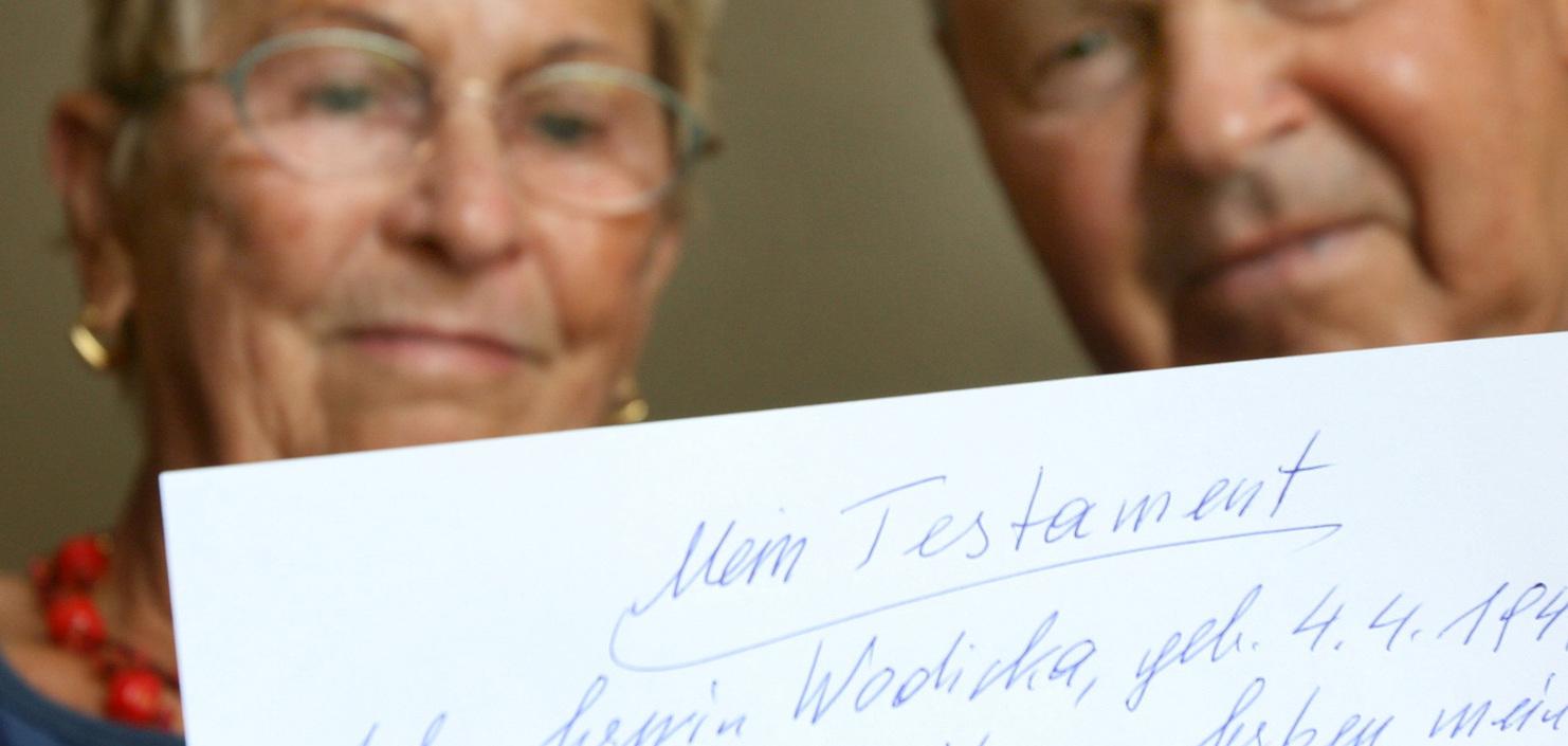 Nahaufnahme eines älteren Paares, das ein handgeschriebenes Testament auf Papier hält.