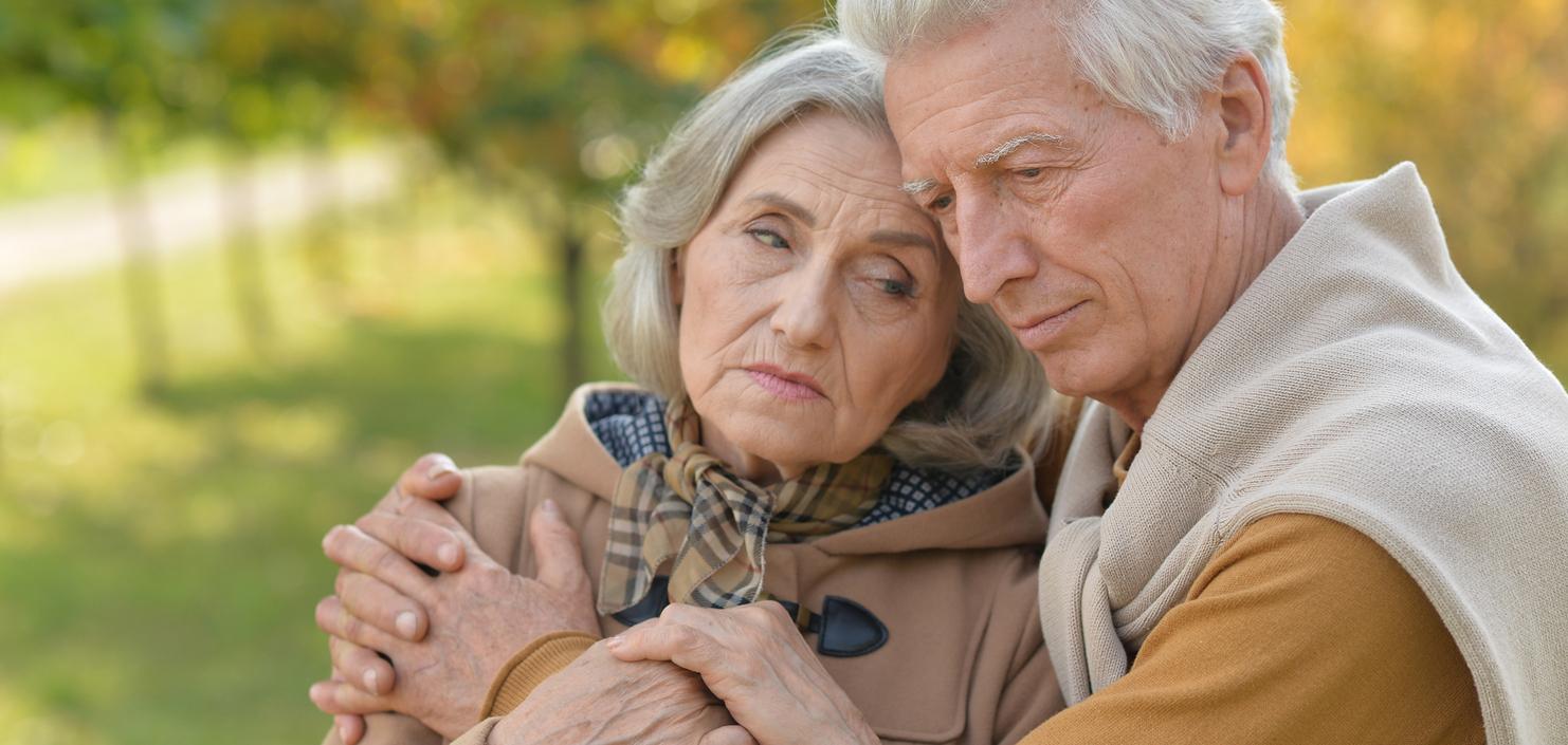 Ein älteres Paar umarmt sich liebevoll, es ist ein herbstlicher Park mit verschwommenem Hintergrund.