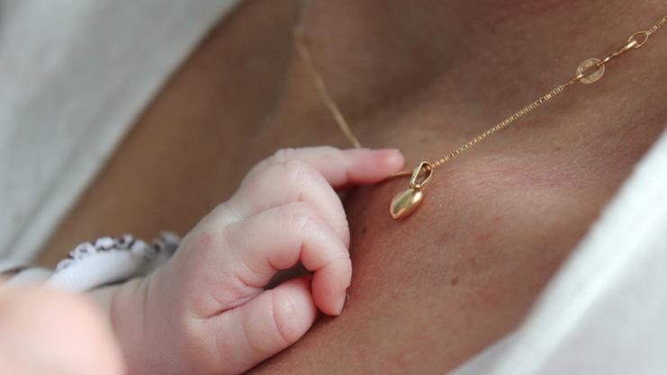 Babyhand greift sanft nach einer goldenen Halskette mit Anhänger auf der Haut einer Person.